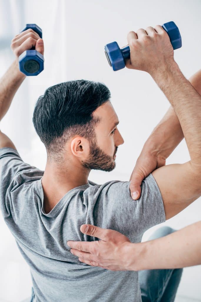 Chiropractor treating a patient's shoulder while he's holding weights.